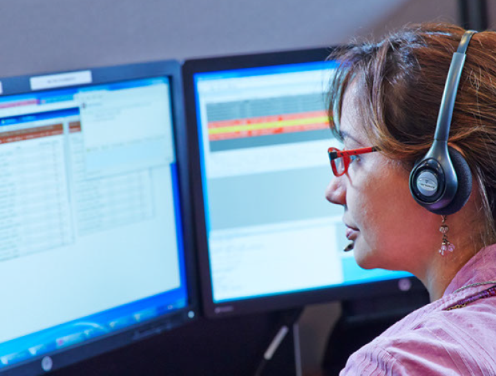 Shows a woman looking at two computer screens wearing a headset