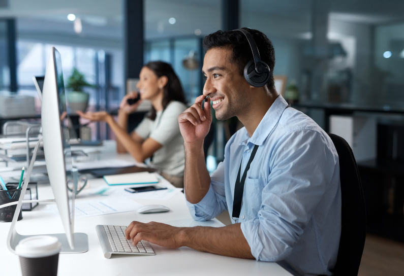 Shows people at their desks talking over a headset and looking at computer screens 