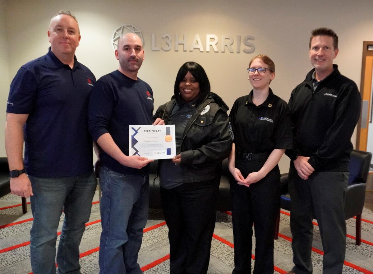 Photo of 5 people facing the camera, with a woman in the center receiving a citation