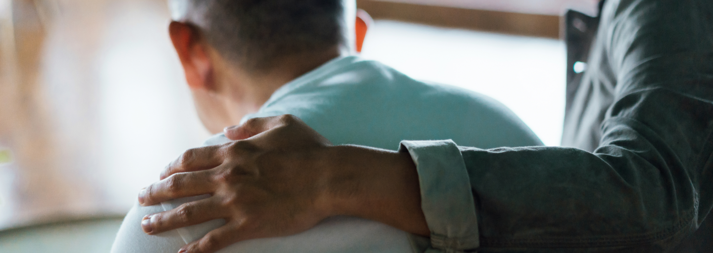 Shows the back of a man with someone's arm around his shoulders