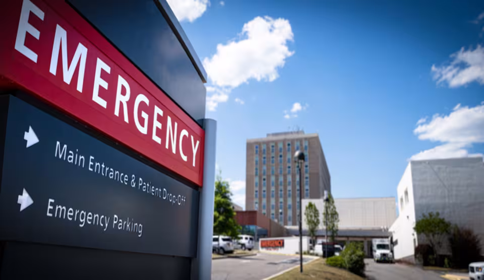 Exterior view of a hospital emergency entrance sign with directional arrows for patient drop-off and parking.