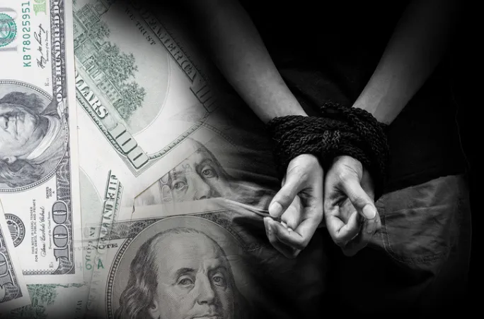 Person’s hands tied in rope over scattered U.S. hundred-dollar bills, illustrating the link between trafficking and illegal profit.