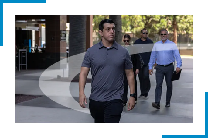 Executive Protection Agent in foreground protecting 2 principals while walking through corporate courtyard, followed by trailing agent. 